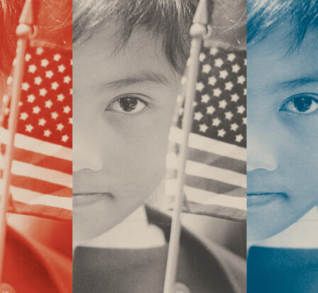 Child holding two small US flags on either side of her face.