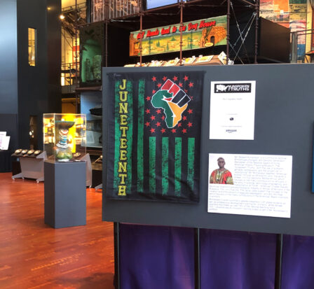 A poster board showing collateral including a Juneteenth flag from Unspoken Truths in the Grand Atrium at MOHAI.