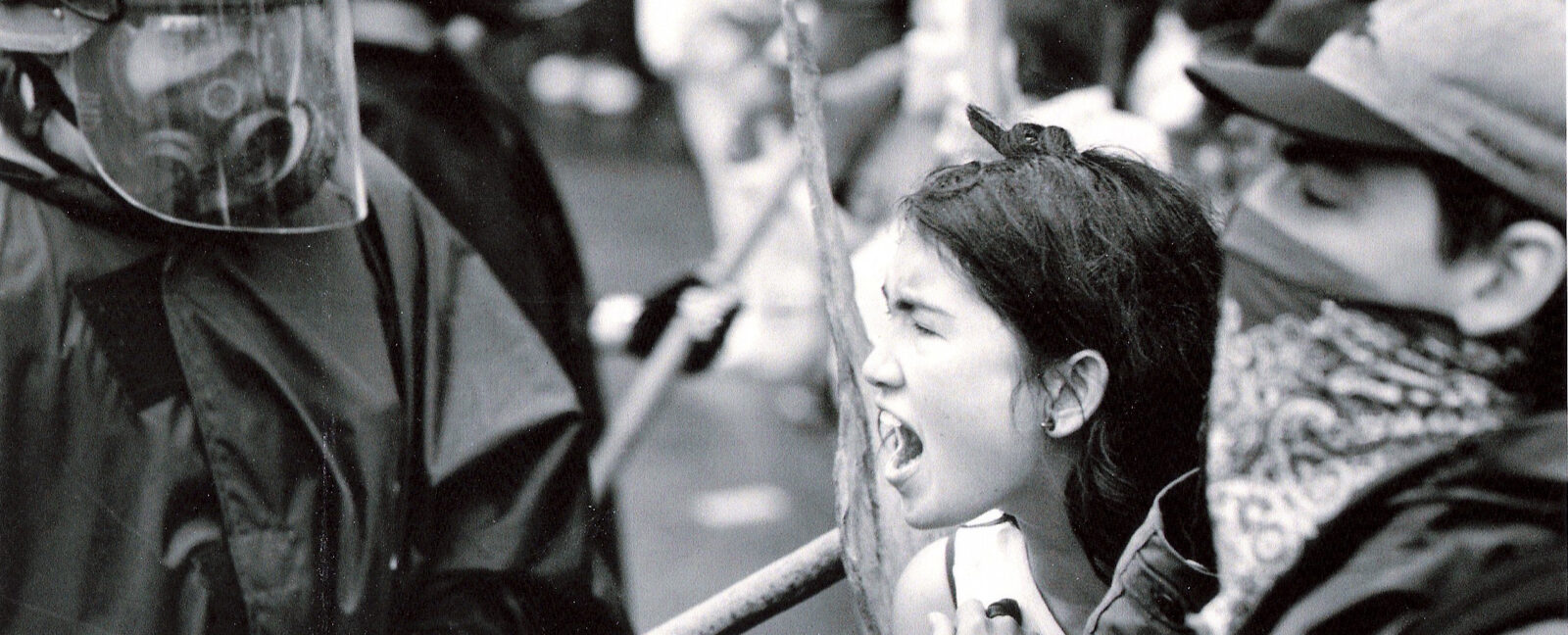 A woman shouting at a person in black combat fatigues wearing a helmet with a clear face shield.