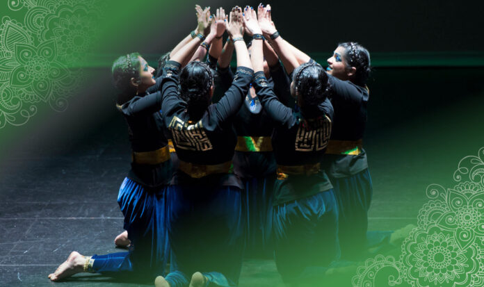 A group of individuals on their knees in a circle with arms raised and meeting above.