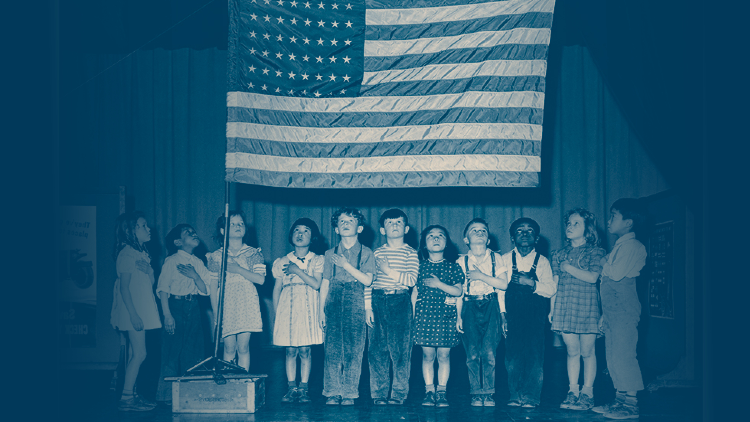 Children with left hands over hearts gazing at US flag.
