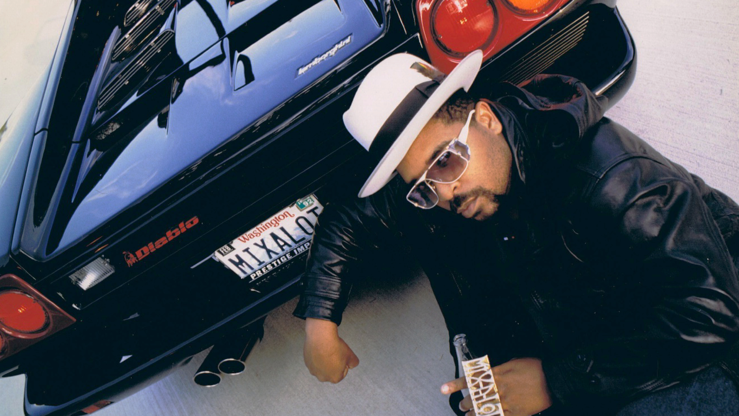 Sir Mix-a-Lot crouching behind a Lamborghini Diablo with a "MIXALOT" Washington license plate.