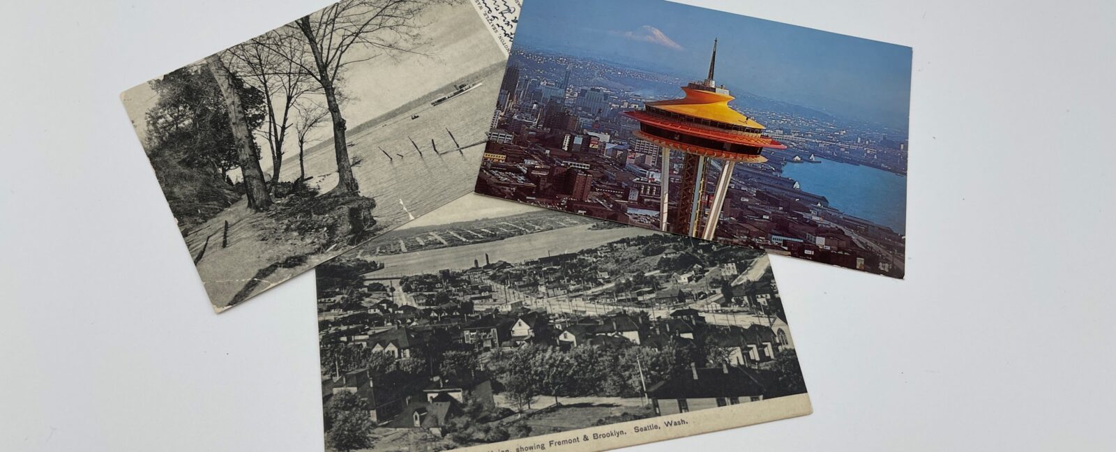 Three postcards showing Seattle through history placed in a neat pile. You can see the Space Needle