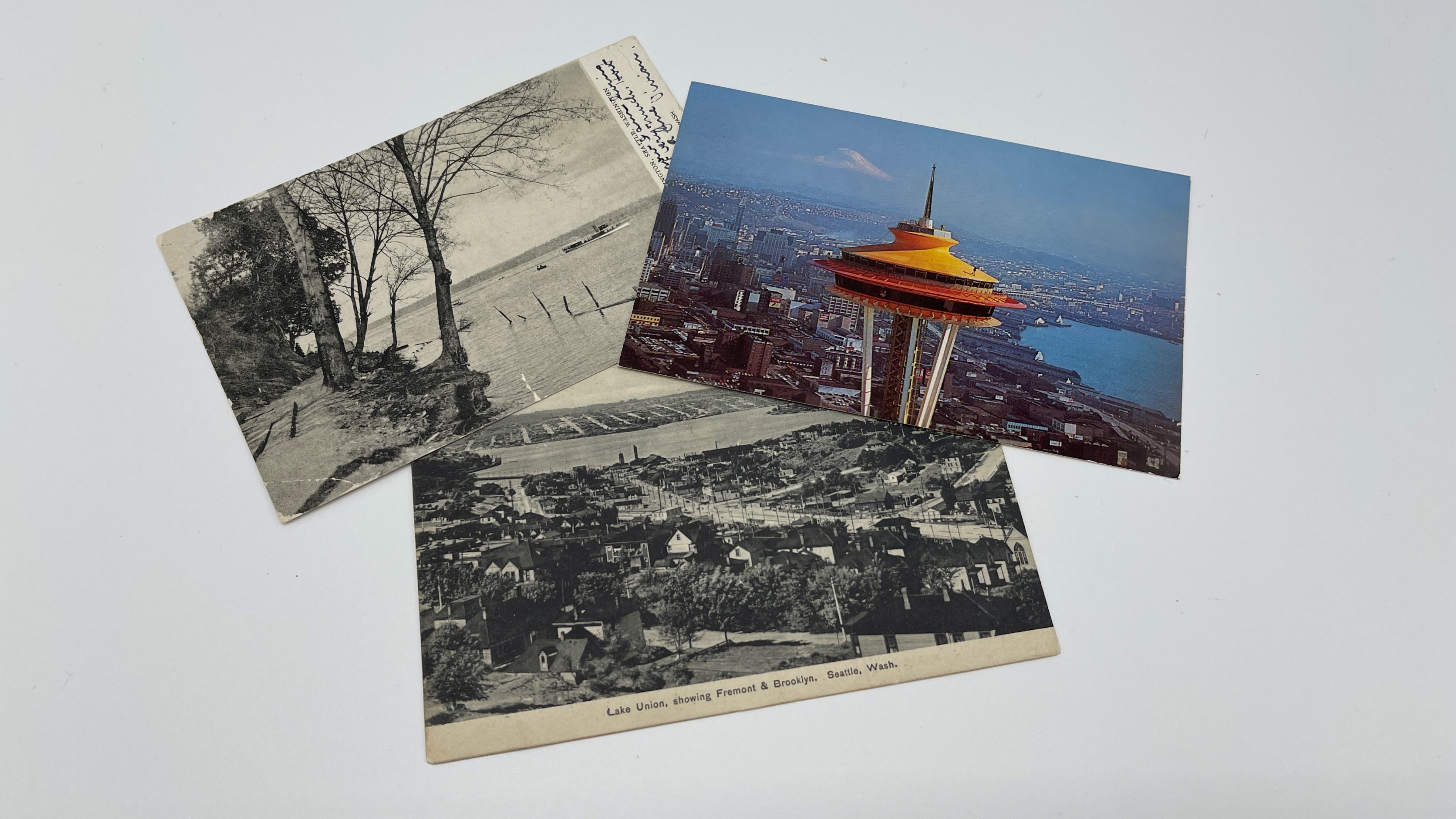 Three postcards showing Seattle through history placed in a neat pile. You can see the Space Needle