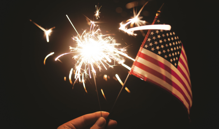 A hand holds a small American Flag and a lit sparkler.