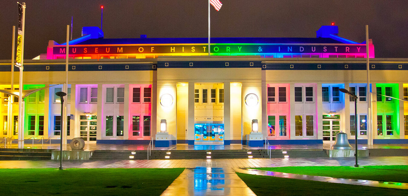 Exterior photo of MOHAI at night lit up in rainbow colors.