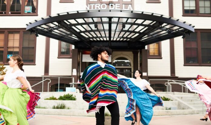 Latino dancers wearing colorful clothing perform traditional dances in front of El Centro de la Raza.