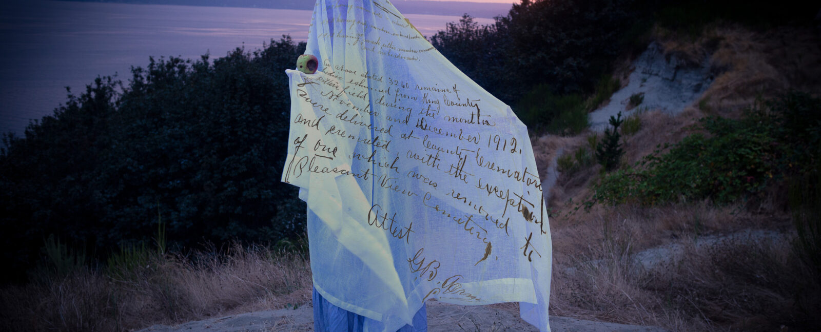 A person stands covered in a white sheet holding an apple.