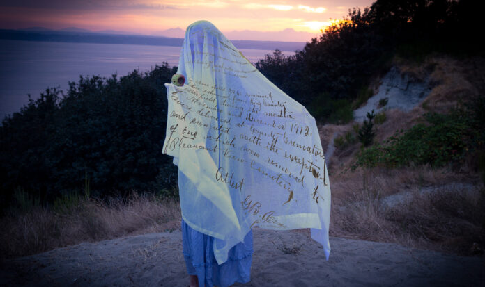 A person stands covered in a white sheet holding an apple.