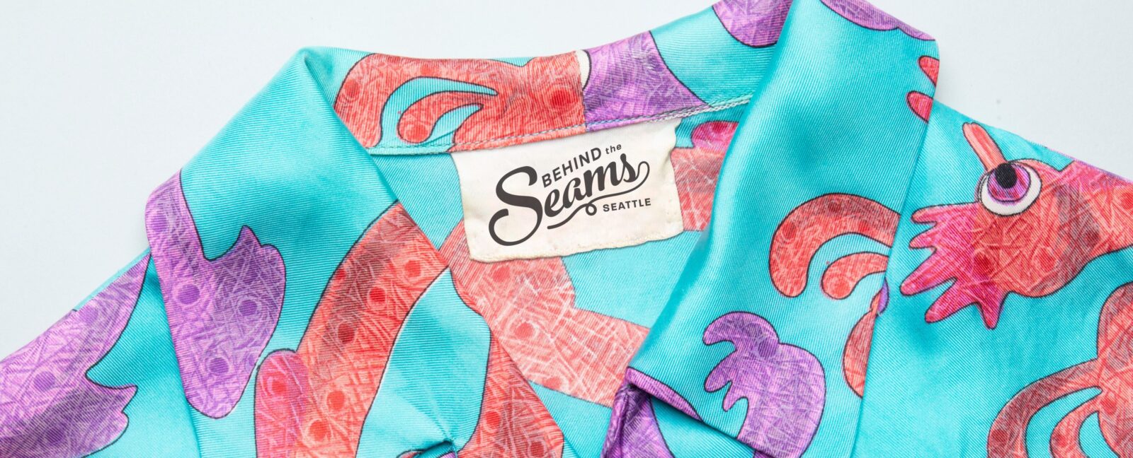 Teal shirt with orange and purple design. Tag reads "Behind the Seams