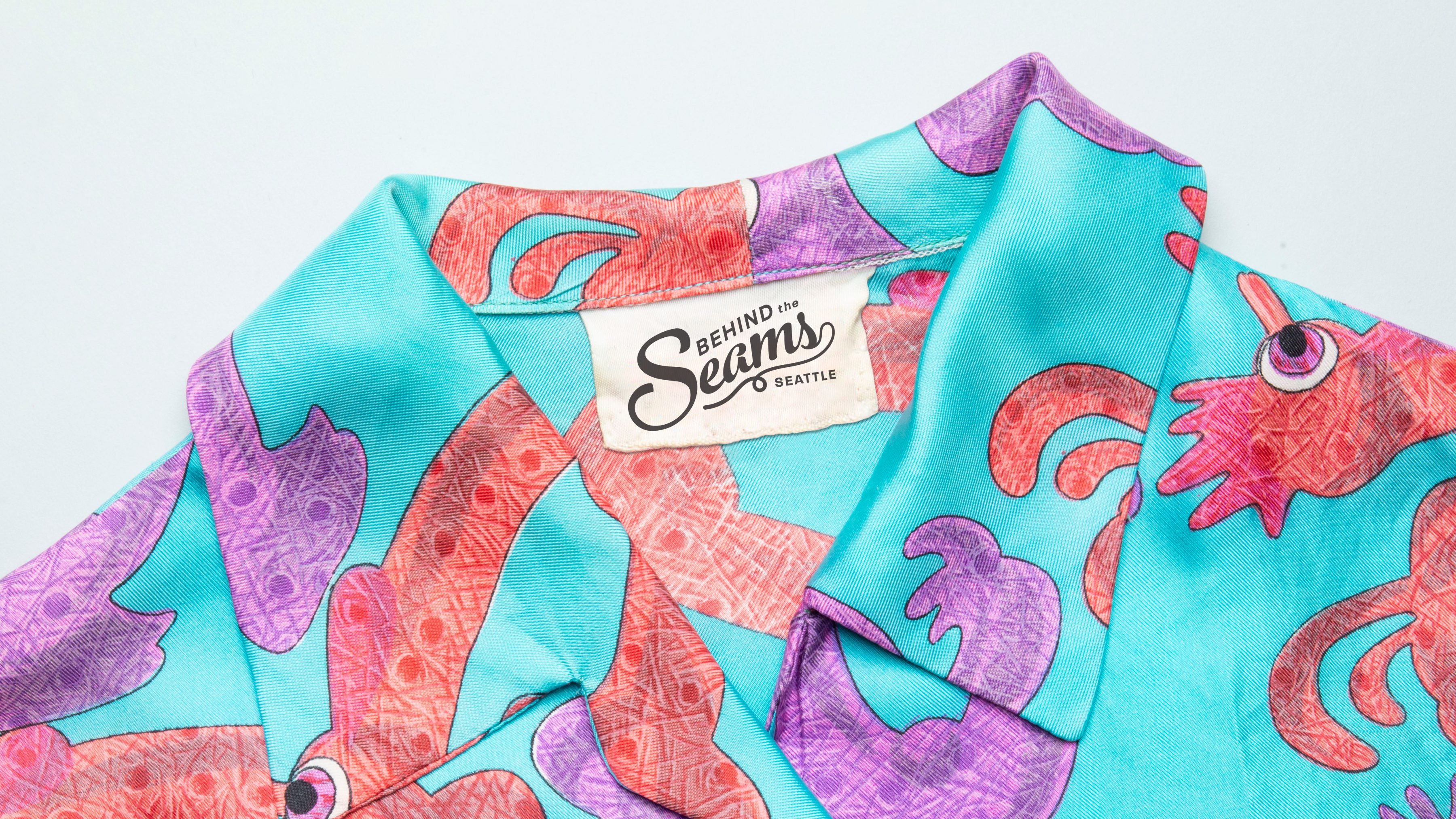 Teal shirt with orange and purple design. Tag reads "Behind the Seams