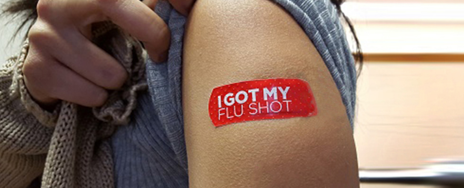 A person pulls up their sleeve to reveal a bandaid that reads "I Got My Flu Shot".
