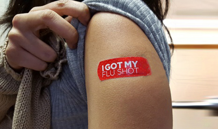 A person pulls up their sleeve to reveal a bandaid that reads "I Got My Flu Shot".