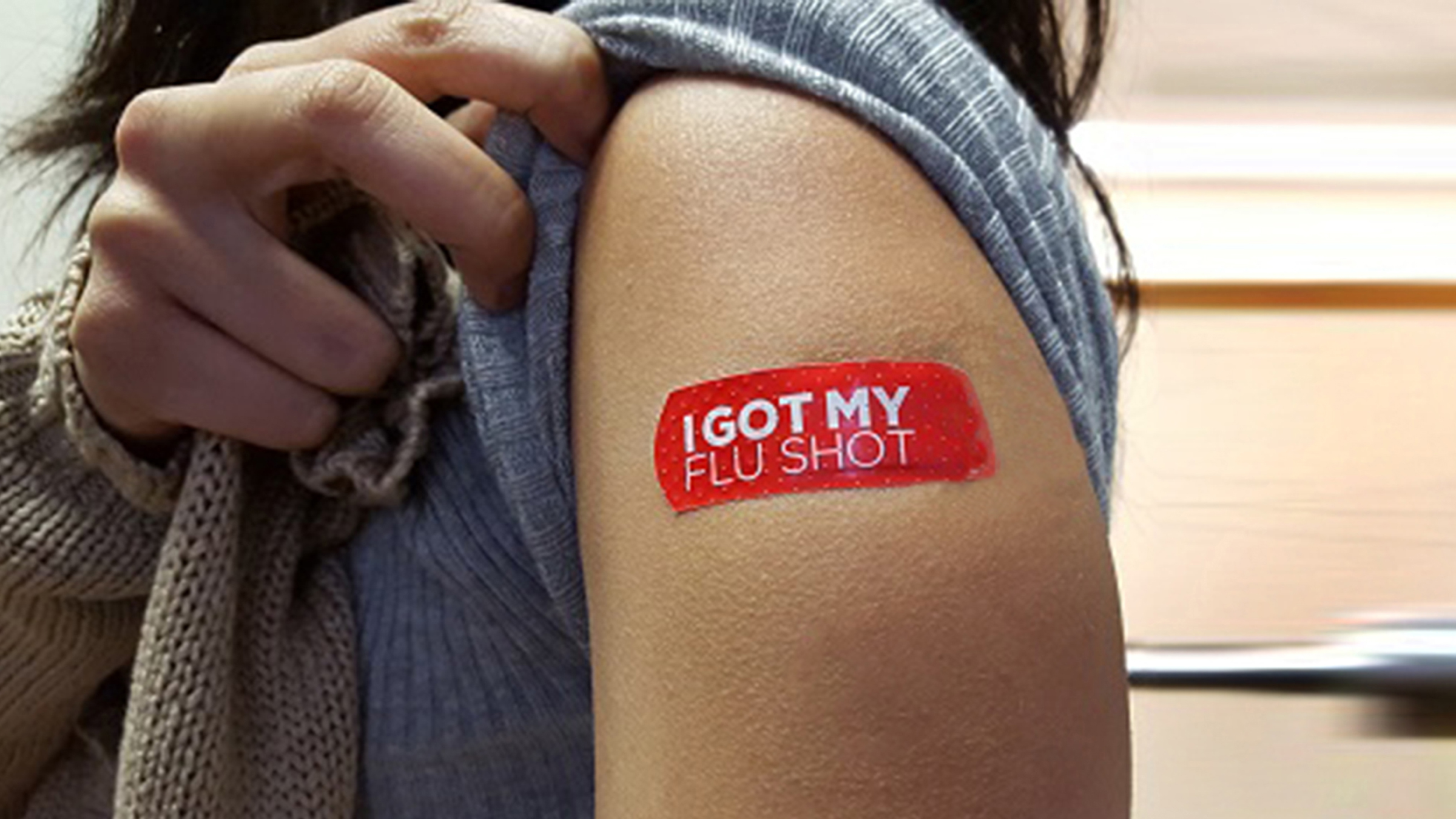A person pulls up their sleeve to reveal a bandaid that reads "I Got My Flu Shot".