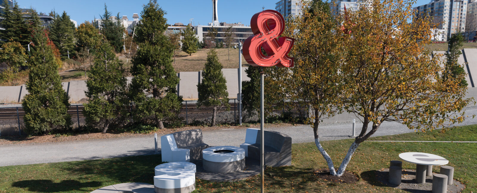 A red ampersand neon sign on a post in downtown Seattle. The Seattle Space Needle can be seen in the background.