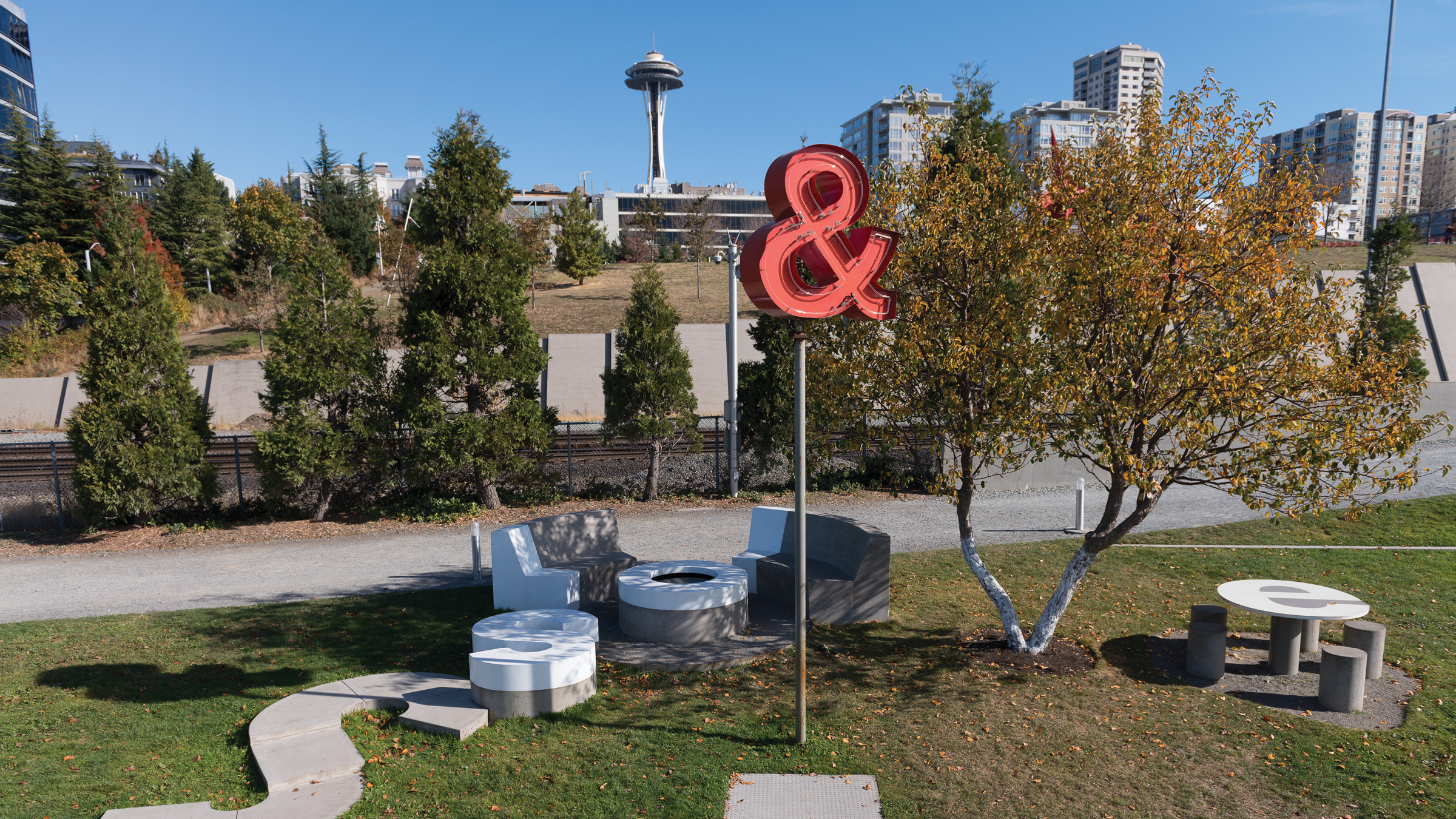 A red ampersand neon sign on a post in downtown Seattle. The Seattle Space Needle can be seen in the background.
