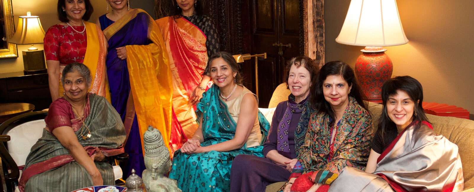 Indian women sit in a living room wearing colorful clothing.