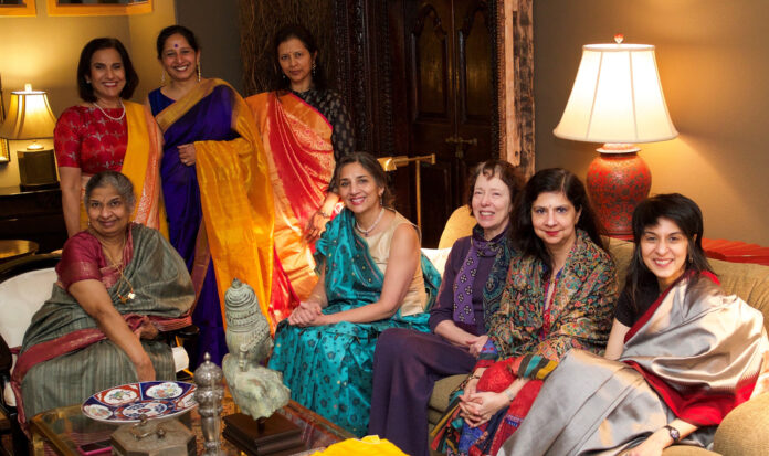 Indian women sit in a living room wearing colorful clothing.