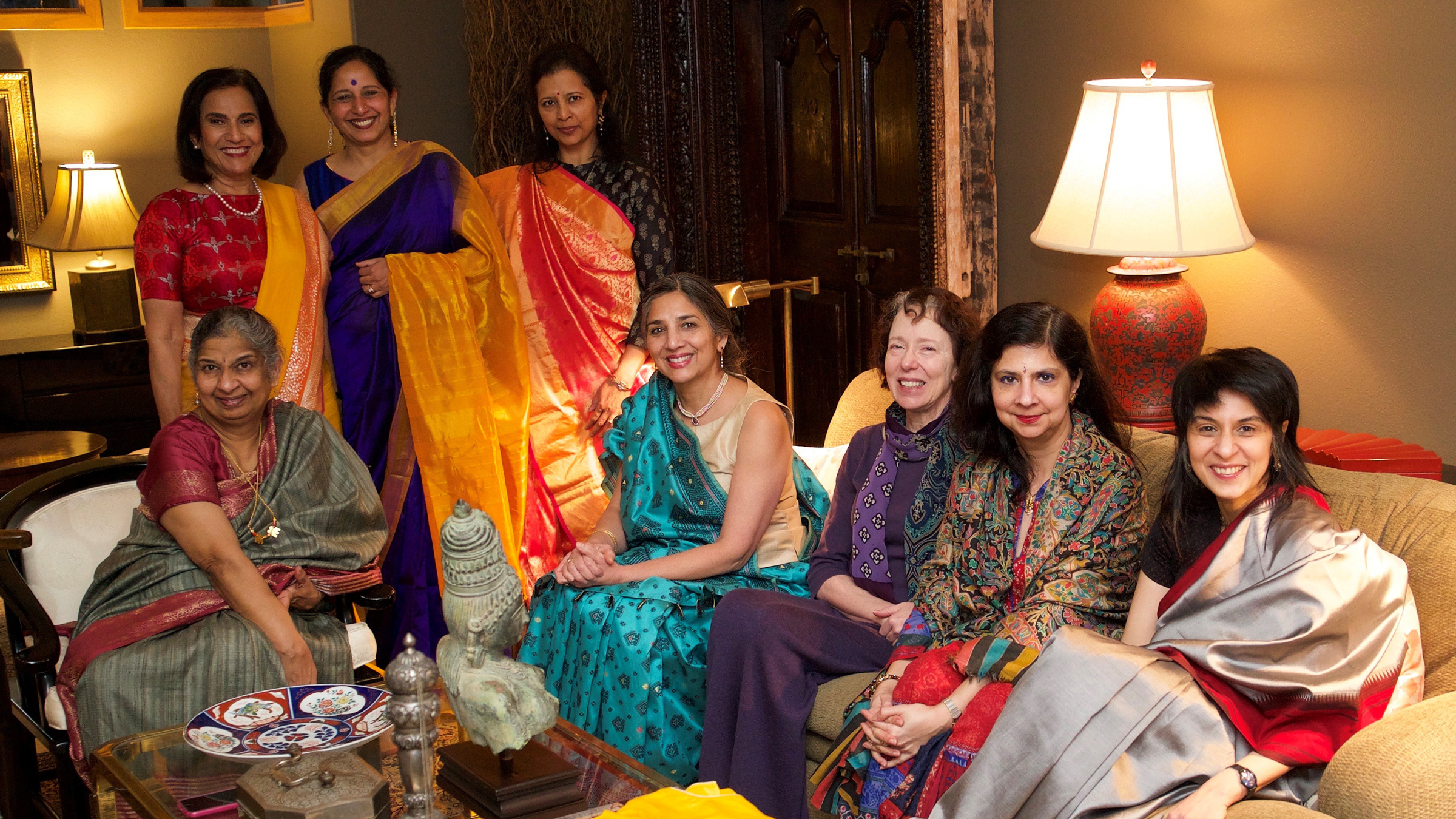 Indian women sit in a living room wearing colorful clothing.