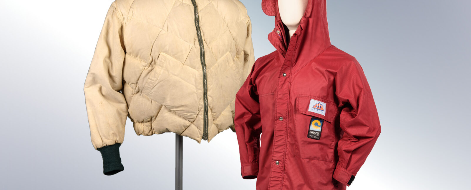 Two coats on display. The left coat is cream colored. The right coat has a hood and is red colored.