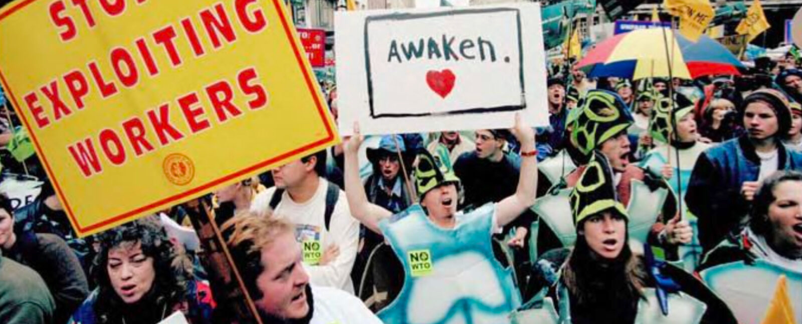 1999 WTO protest march with signs reading "Stop Exploiting Workers" and "Awaken" being held in downtown Seattle