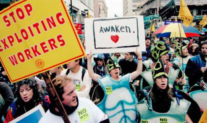 1999 WTO protest march with signs reading "Stop Exploiting Workers" and "Awaken" being held in downtown Seattle