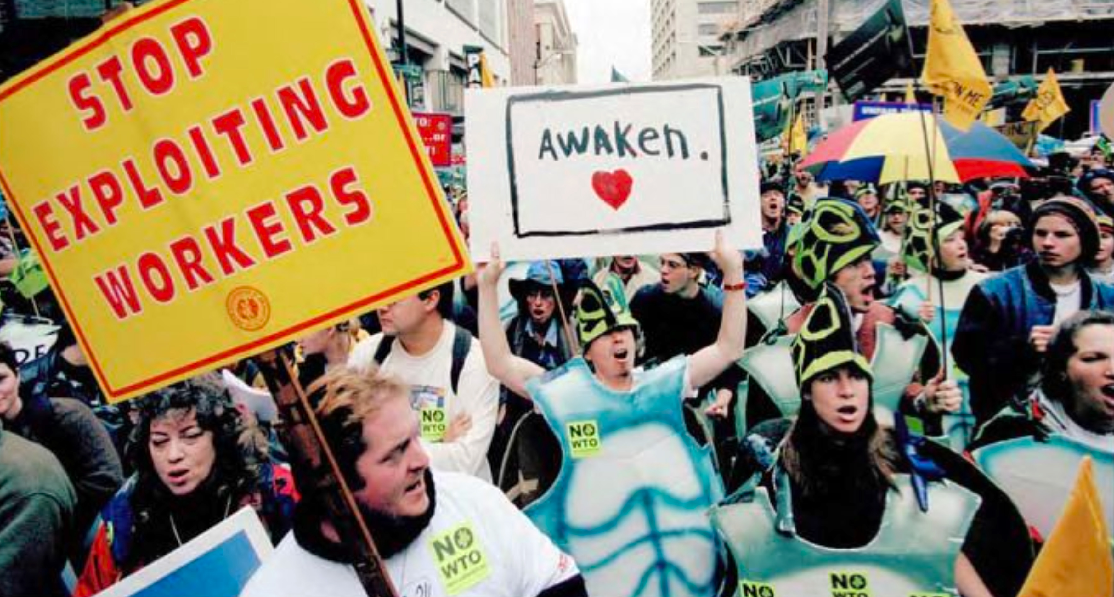 1999 WTO protest march with signs reading "Stop Exploiting Workers" and "Awaken" being held in downtown Seattle