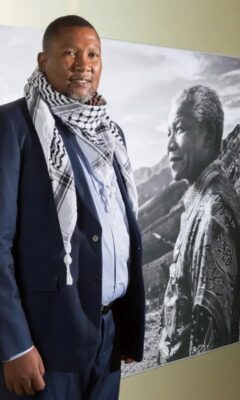 Nkosi Zwelivelile Mandela stands adjacent to a photo of Nelson Mandela.