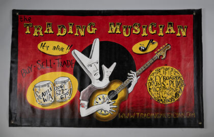 Banner from The Trading Musician, 1999, shows illustration of a two-headed person (heads in the shape of a Gibson Flying V guitar) playing a dobro.