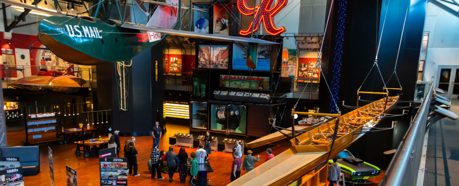 The Grand Atrium at MOHAI. The Husky Challenger and the Boeing B-1 hand from the ceiling. People mill about on the hardwood floor.