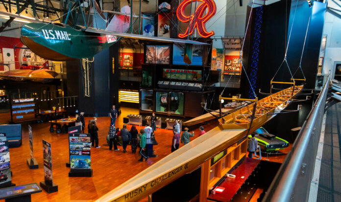 The Grand Atrium at MOHAI. The Husky Challenger and the Boeing B-1 hand from the ceiling. People mill about on the hardwood floor.