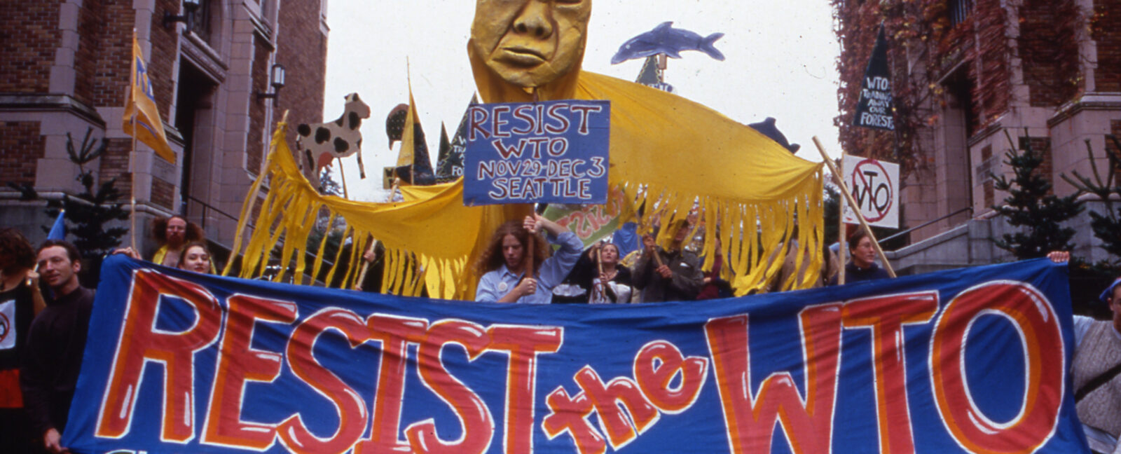 Activists march through Seattle streets during the WTO protests of 1999. A sign reads, "Resist the WTO - Globalize liberation, not corporate power".