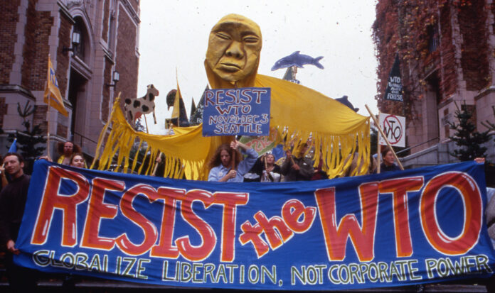 Activists march through Seattle streets during the WTO protests of 1999. A sign reads, "Resist the WTO - Globalize liberation, not corporate power".
