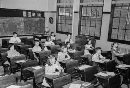 Black and white photograph of a students in a classroom with a handful of empty desks.