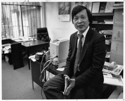 Black and white photograph of Da C. Le sitting on top of a desk in his office.