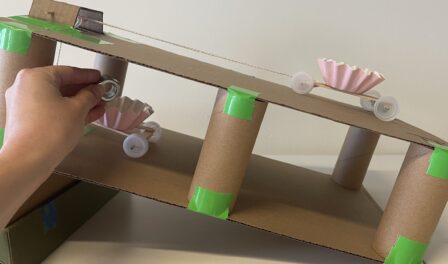 An inclined cardboard ramp with cupcake wrappers on wheels.