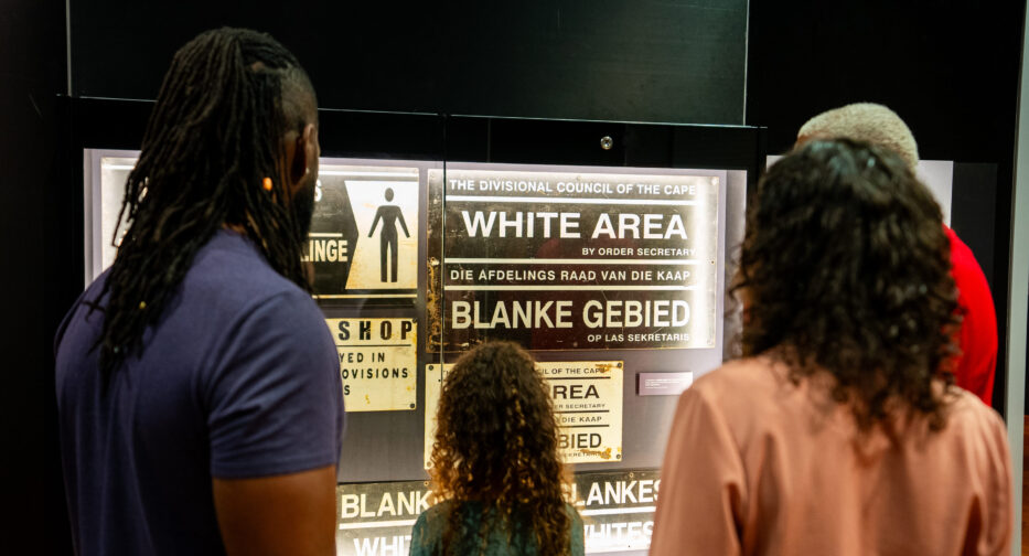 Visitors to Mandela exhibit exploring historical notices that designated spaces by race, reflecting the policies of the apartheid era and providing insight into the social and political climate of the time.