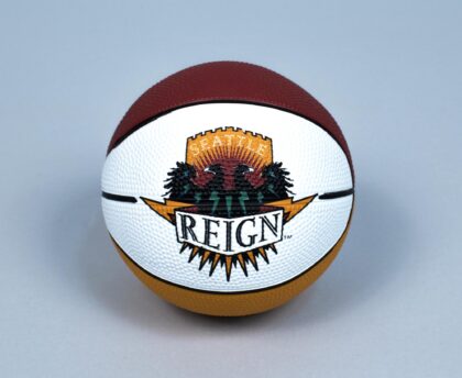 A basketball featuring the Seattle Reign logo from the American Basketball League (ABL). The logo shows two black birds in front of evergreen trees with the words "Seattle Reign" on a gold and white background.