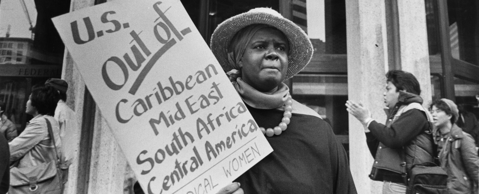 A woman holds a sign reading, "U.S. Out of Caribbean Mid East South Africa Central America Radical Women"