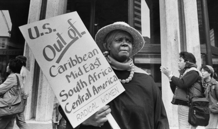 A woman holds a sign reading, "U.S. Out of Caribbean Mid East South Africa Central America Radical Women"