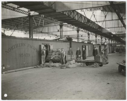 Black and white photograph of seven employees in a warehouse in front of a wall that reads "Northern Pacific."
