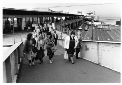 Black and white photograph of a crowd of people disembarking a ferry at the Seattle ferry terminal in the 1980s.