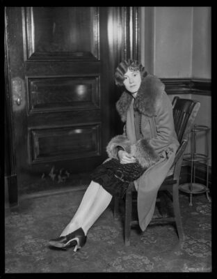 Elise Olmstead seated in front of a fireplace wearing a fur jacket.