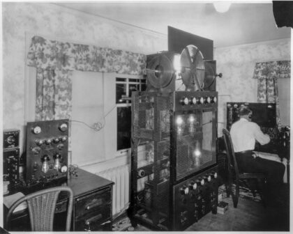 1920s radio broadcasting equipment inside the Olmstead home, showing a man operating the transmitter for KFQX station suspected of sending coded messages during Prohibition.
