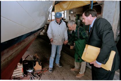 A color photo of Anchor and Dewitt Jensen examining the hull of a boat with an unknown man.