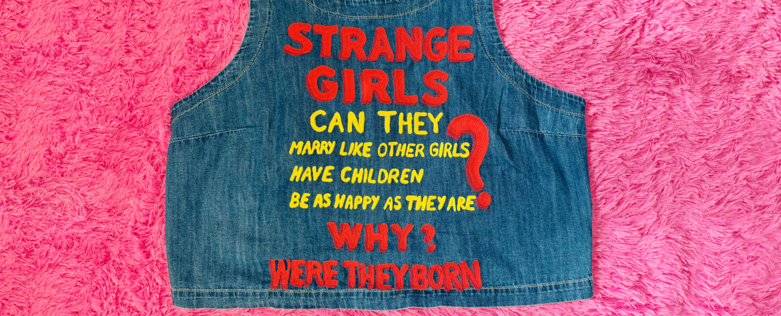 Stiching on a denim shirt reading, "Strange Girls. Can They marry like other girls? Have children? Be as happy as they are? Why were they born?"