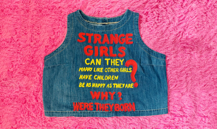 Stiching on a denim shirt reading, "Strange Girls. Can They marry like other girls? Have children? Be as happy as they are? Why were they born?"
