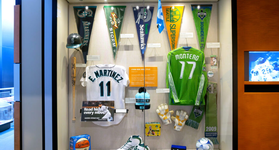 A Seattle sports display at MOHAI showing the jerseys of Edgar Martinez (#11) and Fredy Montero (#17) along with pennants, a basketball, a soccer ball and basketball shoes.