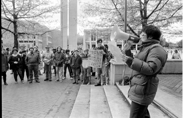 University of Washington students gather in Red Square in 1986 for an anti-apartheid protest, with one speaker using a megaphone and another holding a 