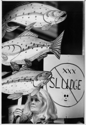 Amanda Van Orden holding a protest sign featuring drawings of three salmon.